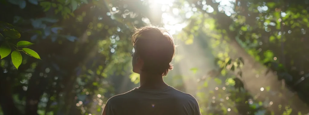 a person stands at the edge of a serene forest, illuminated by soft, dappled sunlight filtering through the leaves, symbolizing hope and emotional healing on the journey to recovery from addiction.